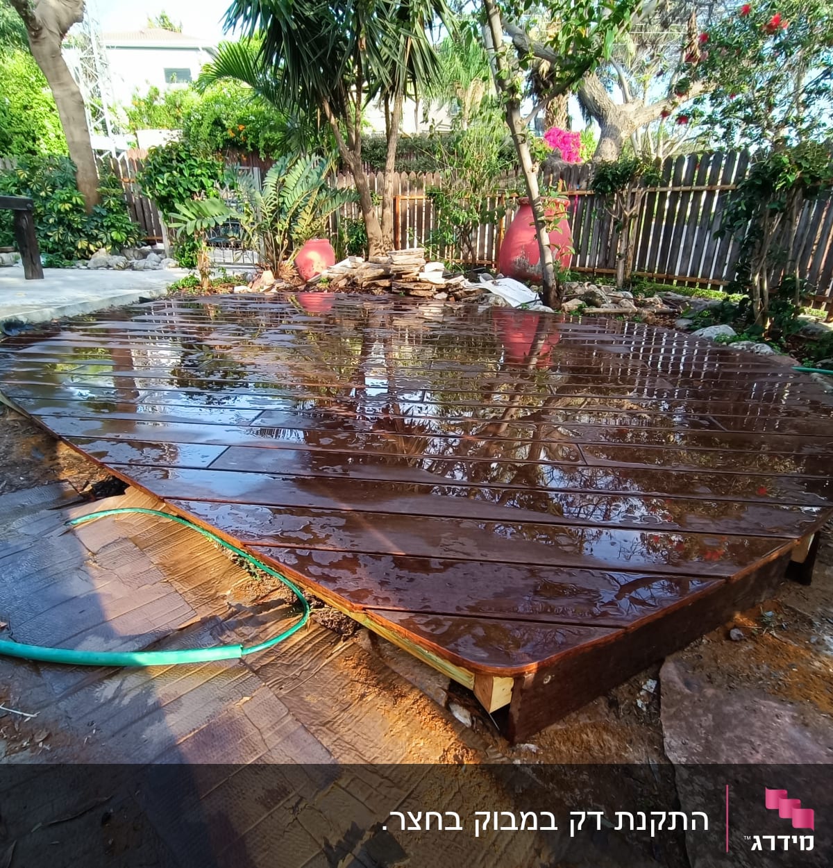 משטח עץ רטוב עם צינור ירוק בגינה